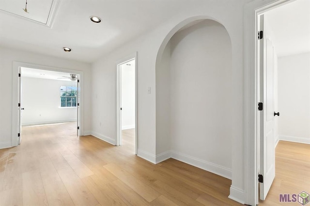 hallway featuring arched walkways, baseboards, recessed lighting, and light wood-style floors