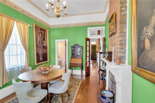 dining room with a healthy amount of sunlight, a brick fireplace, hardwood / wood-style flooring, and a notable chandelier