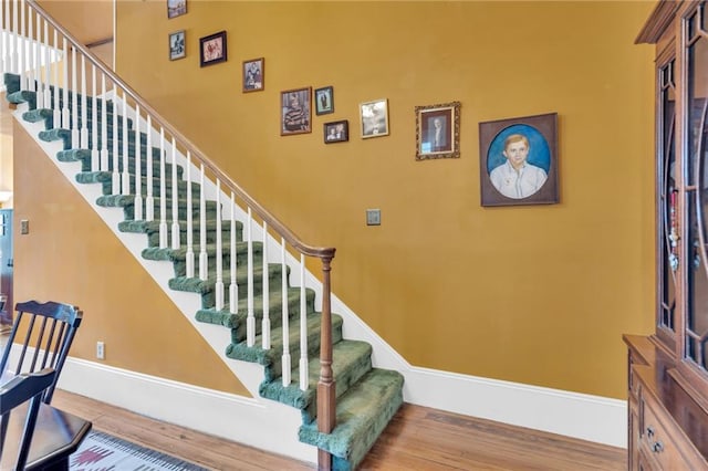stairway featuring baseboards, a high ceiling, and wood finished floors