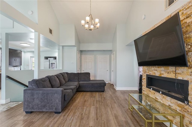 living area featuring an inviting chandelier, visible vents, wood finished floors, a stone fireplace, and high vaulted ceiling
