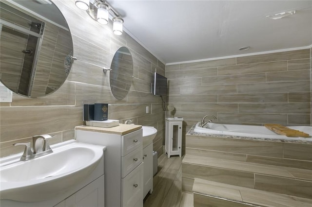 bathroom with a garden tub, crown molding, tile walls, two vanities, and a sink