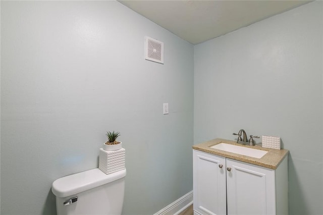 half bathroom featuring vanity, baseboards, toilet, and visible vents