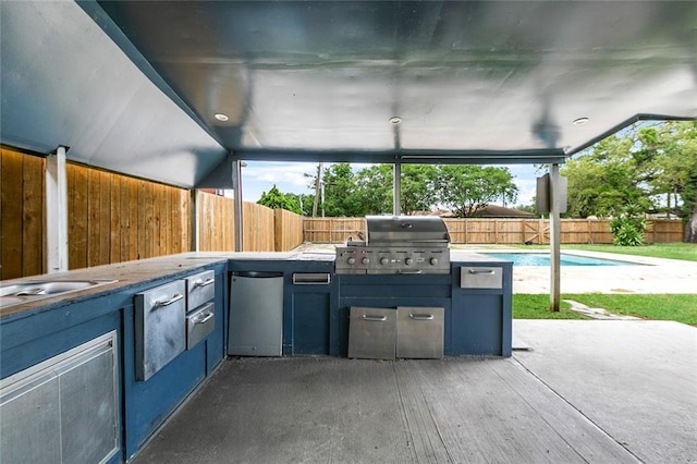 view of patio with area for grilling, exterior kitchen, a fenced in pool, and a fenced backyard