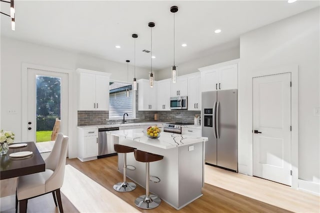 kitchen featuring decorative backsplash, a kitchen island, light wood-type flooring, white cabinets, and stainless steel appliances