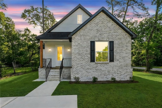 view of front of house featuring brick siding, a yard, and covered porch