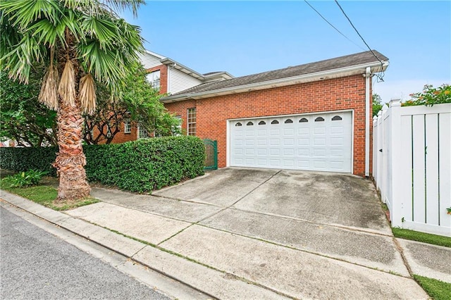 exterior space featuring fence, roof with shingles, brick siding, an attached garage, and driveway