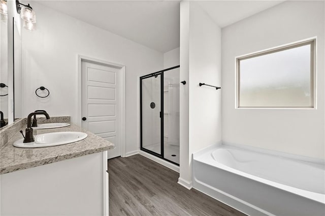 full bath with double vanity, a bath, a shower stall, wood finished floors, and baseboards