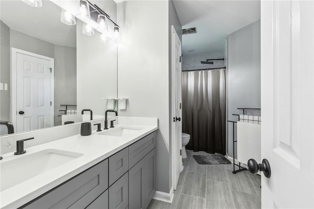 full bathroom featuring double vanity, a sink, baseboards, and toilet