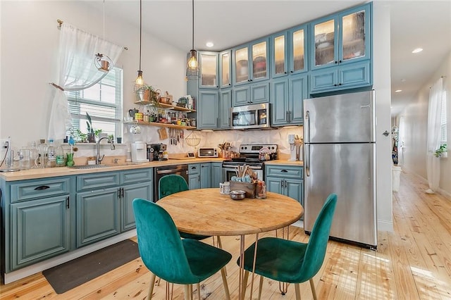 kitchen with hanging light fixtures, a sink, light countertops, stainless steel appliances, and light wood-type flooring