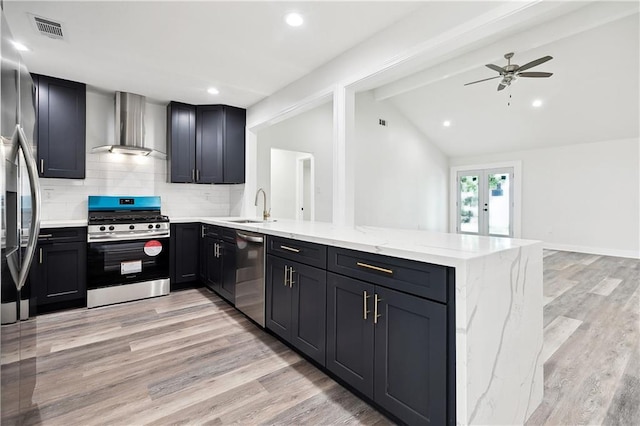 kitchen with visible vents, a peninsula, wall chimney range hood, a sink, and stainless steel appliances