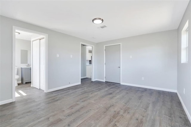 unfurnished bedroom featuring baseboards, visible vents, wood finished floors, and ensuite bathroom