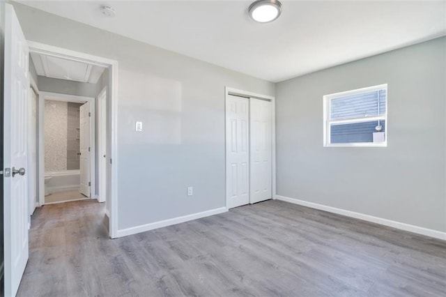 unfurnished bedroom with a closet, attic access, baseboards, and wood finished floors