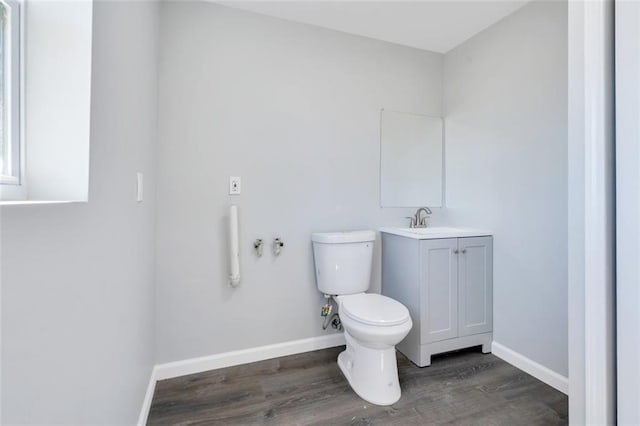 half bathroom featuring toilet, baseboards, wood finished floors, and vanity