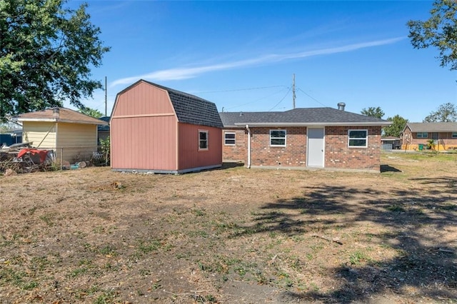 rear view of house with fence, a gambrel roof, brick siding, an outdoor structure, and a yard