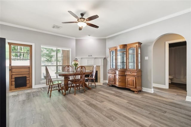 dining space featuring visible vents, a ceiling fan, baseboards, light wood-style floors, and arched walkways