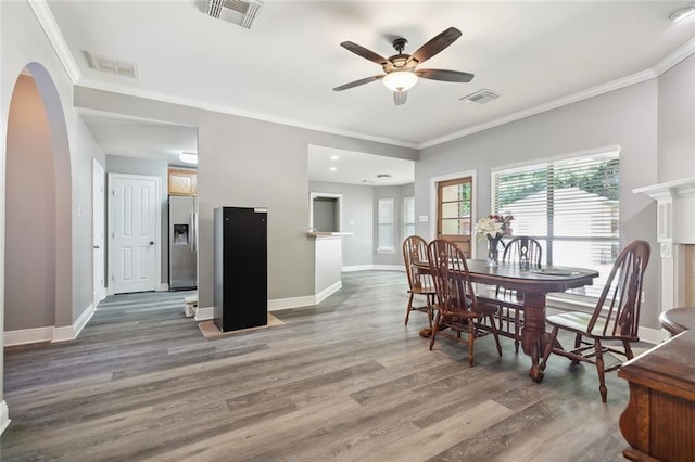 dining space featuring ceiling fan, arched walkways, wood finished floors, visible vents, and ornamental molding