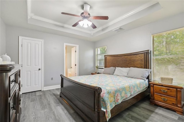 bedroom with visible vents, ornamental molding, wood finished floors, ensuite bathroom, and a raised ceiling