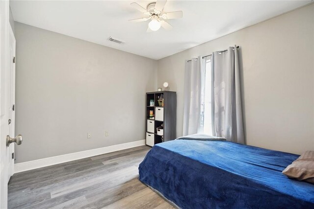 bedroom with visible vents, a ceiling fan, baseboards, and wood finished floors