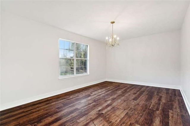 spare room featuring dark wood-style flooring, baseboards, and an inviting chandelier