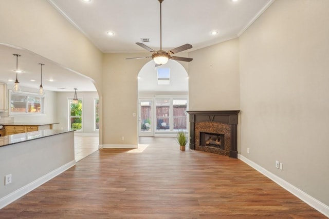 unfurnished living room with arched walkways, a ceiling fan, recessed lighting, wood finished floors, and ornamental molding