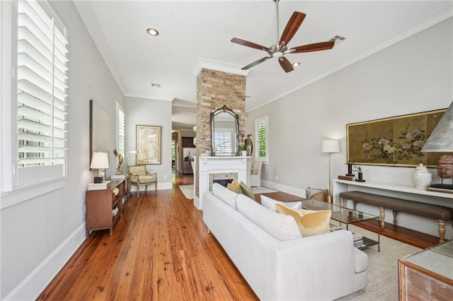 living area with crown molding, ceiling fan, baseboards, wood finished floors, and visible vents