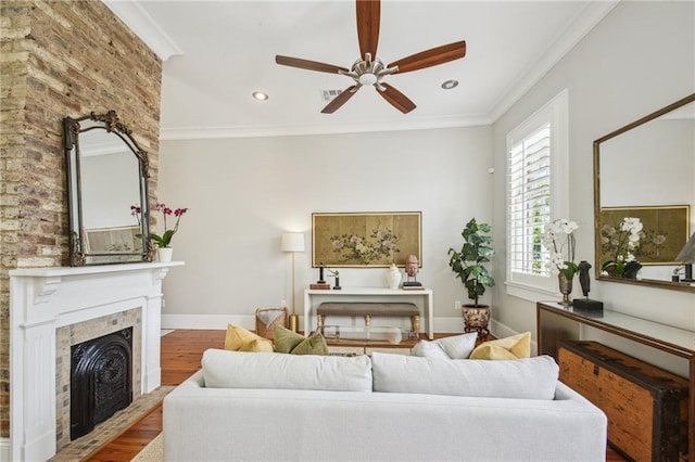 living room featuring crown molding, a fireplace, a ceiling fan, baseboards, and wood finished floors