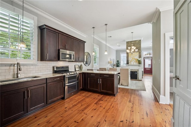 kitchen featuring dark brown cabinets, appliances with stainless steel finishes, a sink, light wood finished floors, and a peninsula
