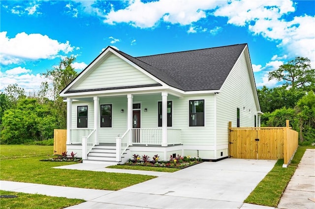 bungalow-style home with a porch, driveway, roof with shingles, and a front lawn