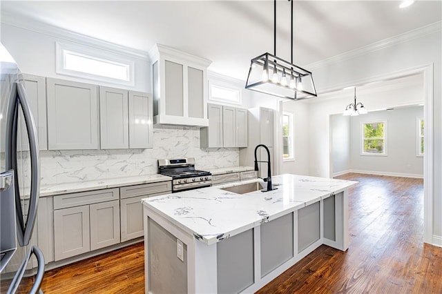 kitchen featuring an inviting chandelier, an island with sink, a sink, backsplash, and stainless steel appliances