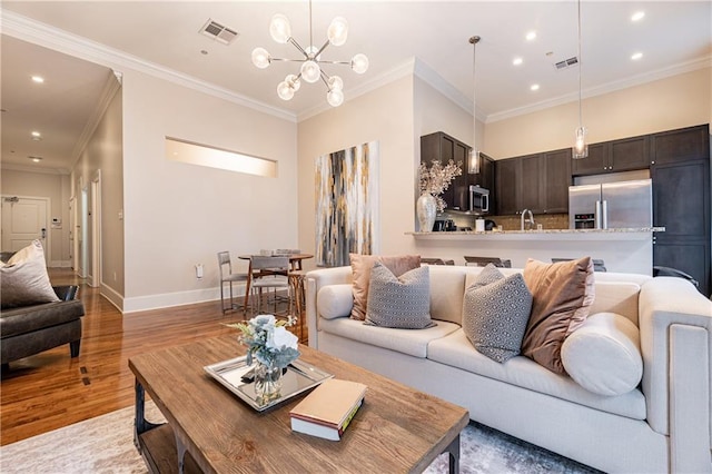 living room featuring an inviting chandelier, ornamental molding, light wood finished floors, and visible vents