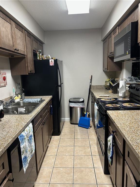 kitchen with dark brown cabinets, a sink, light tile patterned floors, black range with electric cooktop, and dishwashing machine