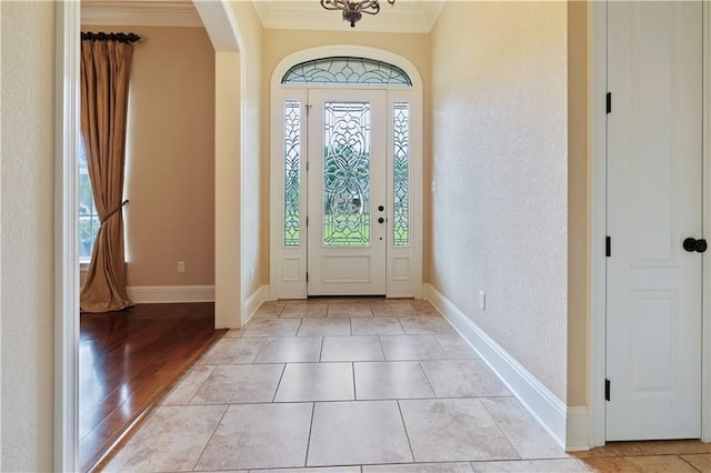 foyer entrance with a textured wall, arched walkways, light wood-style flooring, baseboards, and ornamental molding
