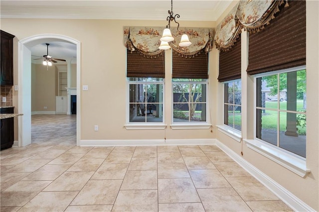 unfurnished dining area featuring ornamental molding, baseboards, arched walkways, ceiling fan with notable chandelier, and light tile patterned floors