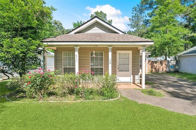 bungalow with covered porch, a front yard, fence, and roof with shingles