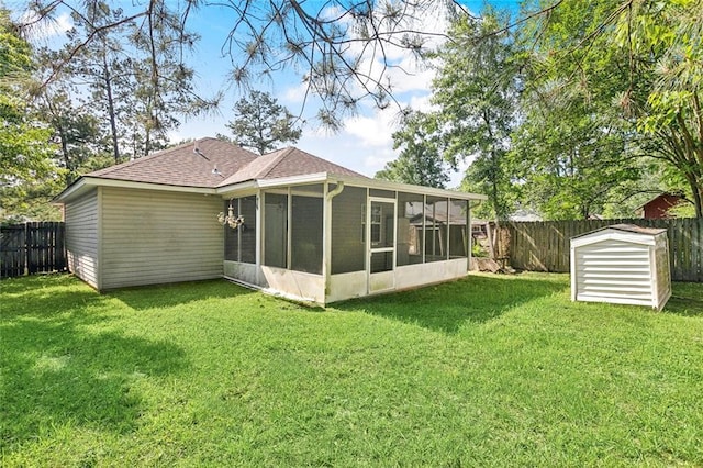 rear view of house featuring a fenced backyard, a yard, a storage unit, and a sunroom
