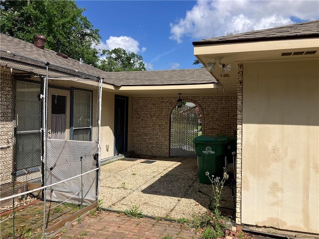 doorway to property featuring visible vents, a shingled roof, and brick siding