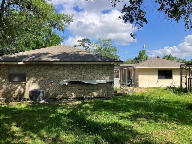 view of home's exterior featuring a lawn, roof with shingles, brick siding, and cooling unit