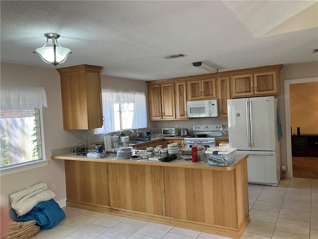 kitchen with brown cabinetry, a textured ceiling, a peninsula, and white appliances