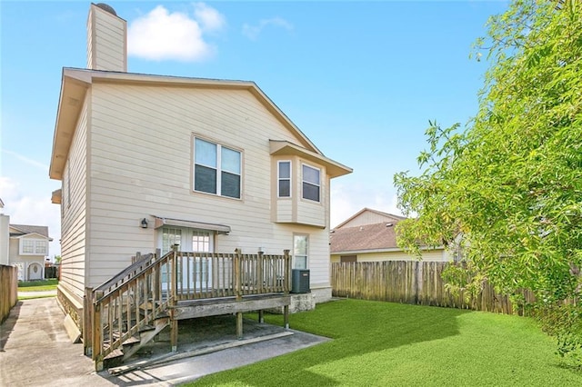 rear view of property featuring a yard, a chimney, a fenced backyard, and central air condition unit