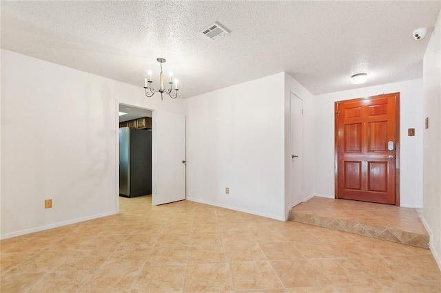 foyer featuring a notable chandelier, a textured ceiling, baseboards, light tile patterned floors, and visible vents
