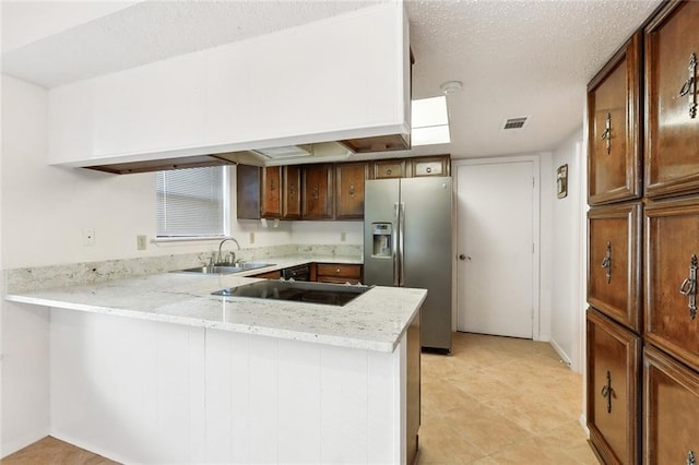 kitchen with a peninsula, stovetop, stainless steel fridge with ice dispenser, light stone counters, and a sink