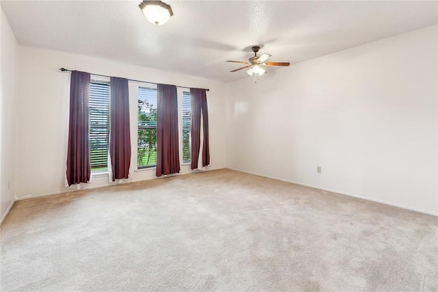 empty room featuring a ceiling fan, baseboards, and light carpet