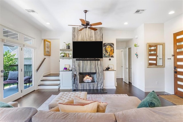living room with a ceiling fan, visible vents, a large fireplace, stairs, and dark wood-type flooring