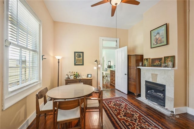 dining area with a tiled fireplace, a ceiling fan, and dark wood finished floors