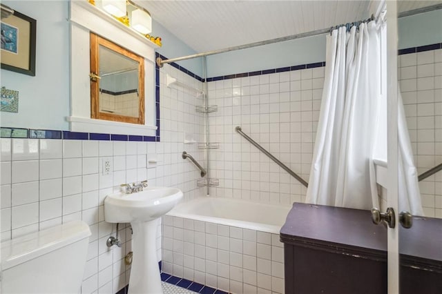 bathroom featuring tiled shower / bath combo, toilet, and tile walls