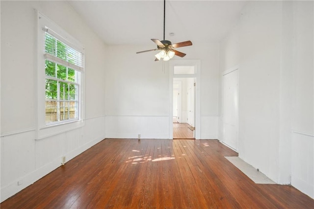 empty room featuring a wainscoted wall, wood-type flooring, and a ceiling fan