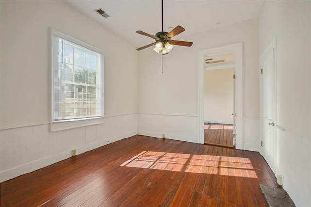 unfurnished room featuring a ceiling fan, visible vents, wainscoting, and hardwood / wood-style flooring