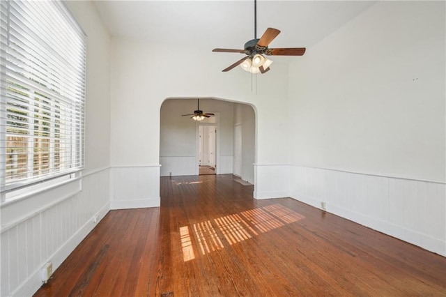 empty room with arched walkways, wainscoting, ceiling fan, and hardwood / wood-style flooring