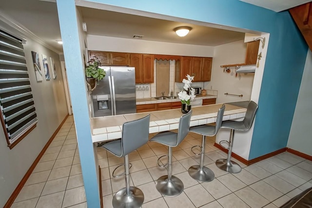 2441 Chartres St, New Orleans, LA 70117 - kitchen with brown cabinetry, a sink, baseboards, tile counters, and stainless steel appliances