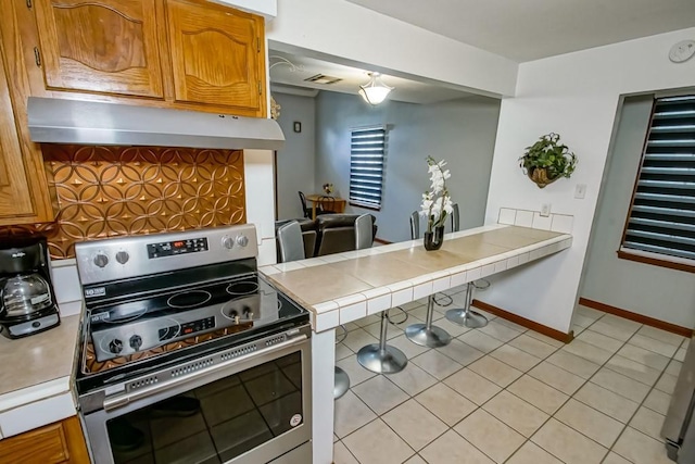 2441 Chartres St, New Orleans, LA 70117 - kitchen featuring tile countertops, visible vents, stainless steel range with electric cooktop, light tile patterned floors, and under cabinet range hood